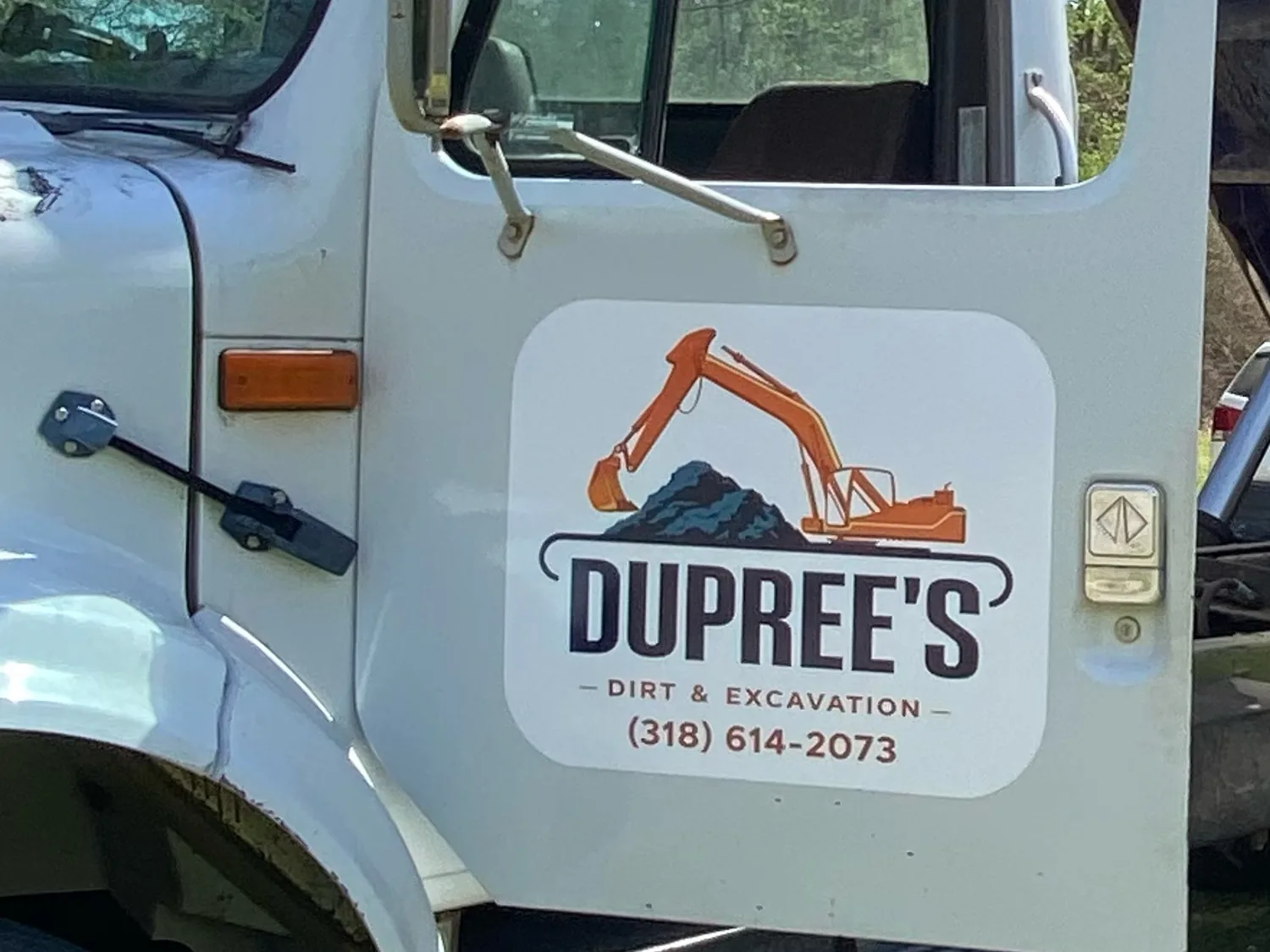 White dump truck with the Dupree's Dirt and Excavation logo and phone number on the door, bed raised behind