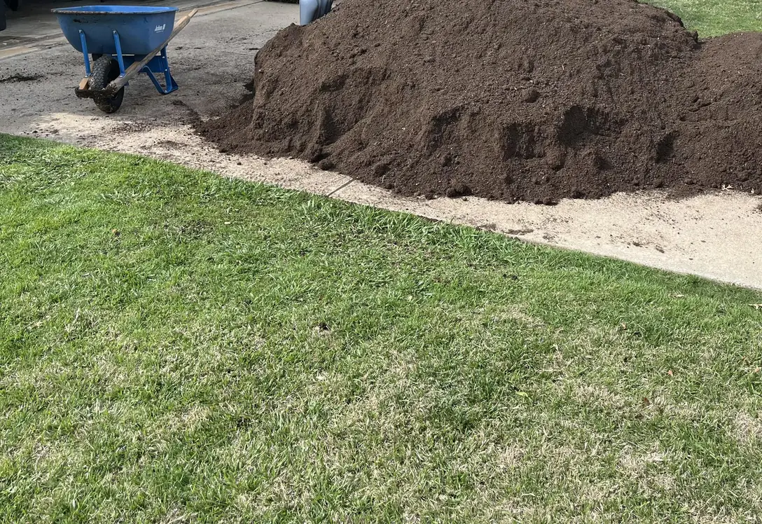 Delivered load of dark topsoil piled at the end of a driveway on a grass yard