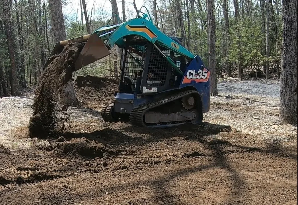 Compact track loader tipping a bucket of dirt out to spread a delivered load