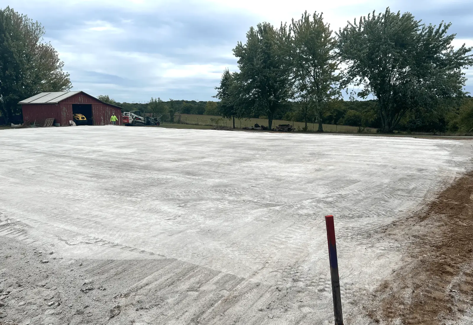 Wide pad of freshly spread crushed limestone running back to a barn at the treeline